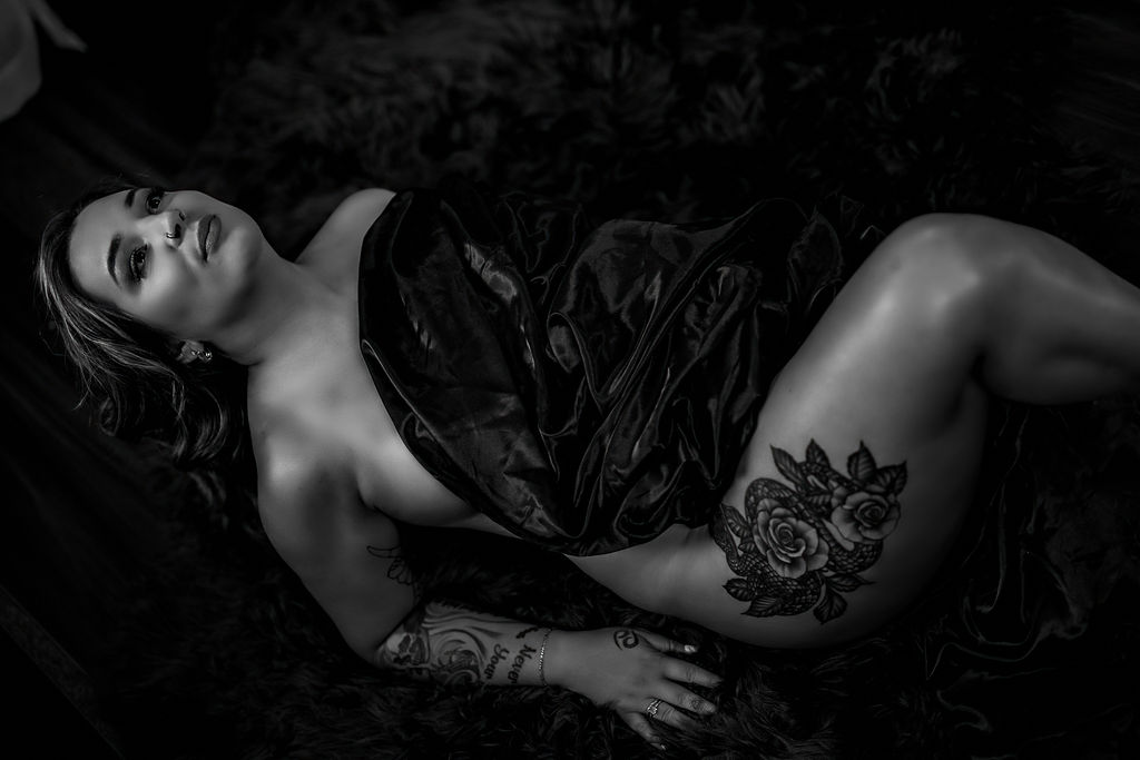 A woman with a rose tattoo on her thigh lays on a floor wrapped in a black blanket botox in annapolis
