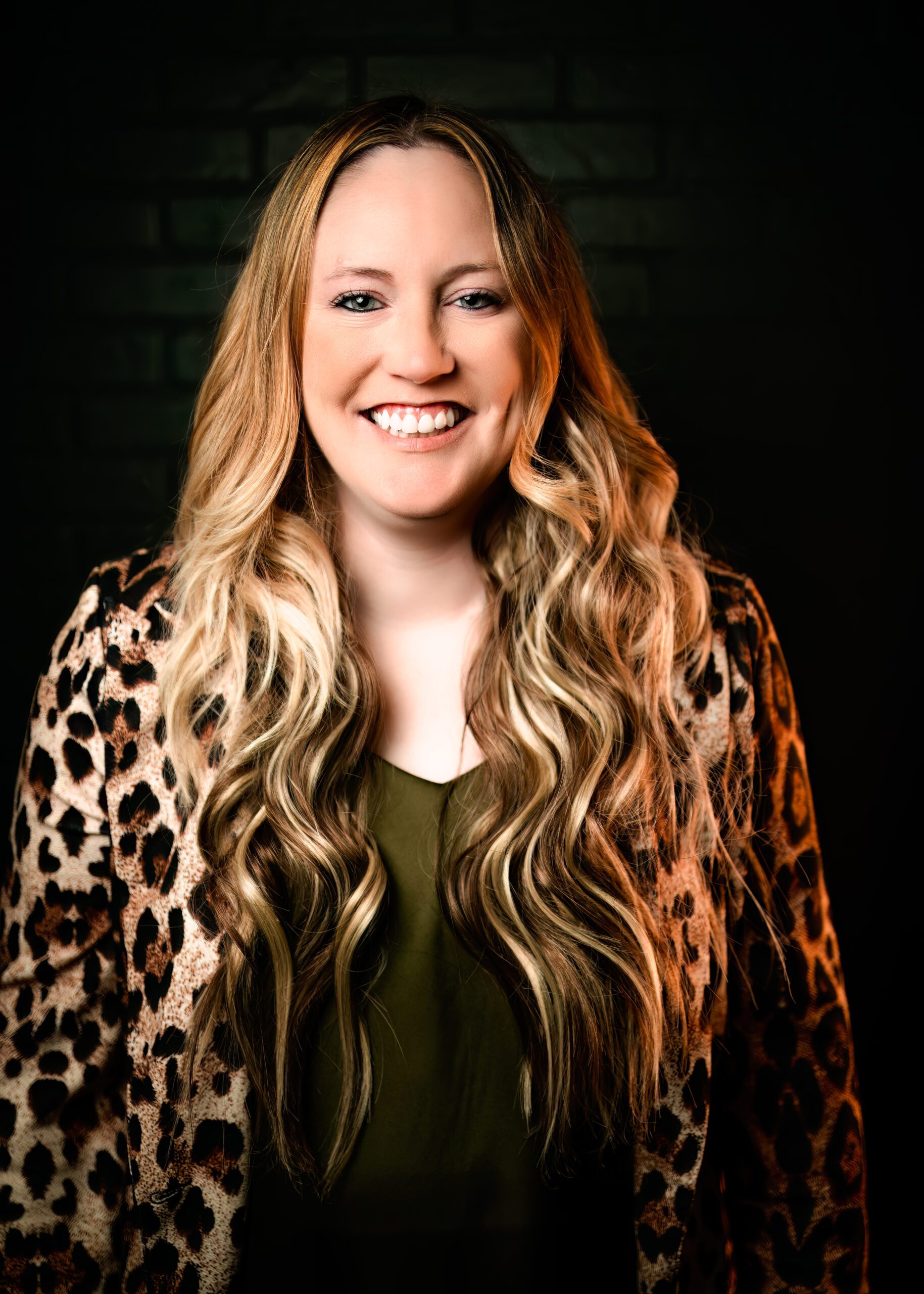 professional headshot of woman smiling against black backdrop wearing leopard blazer