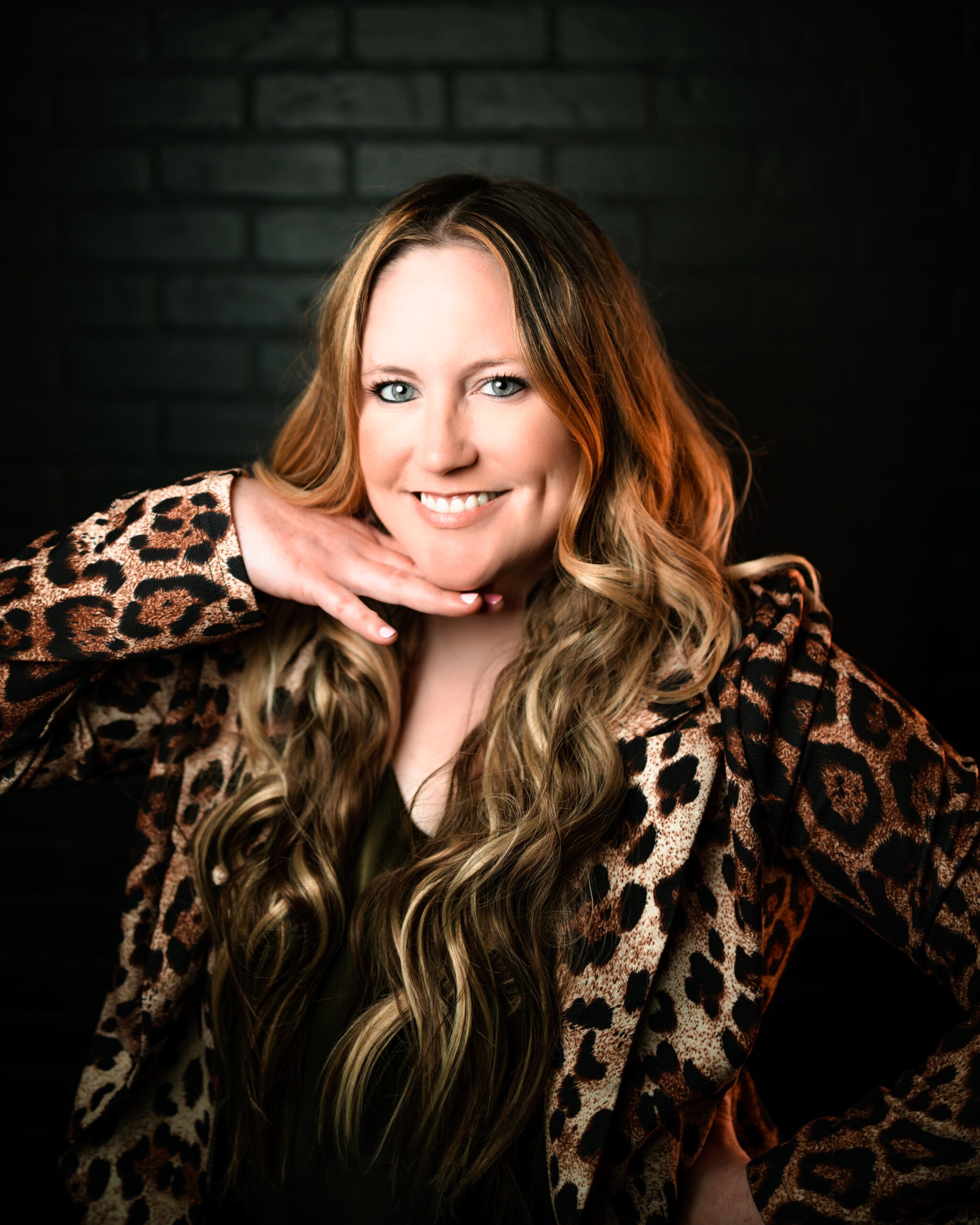 professional headshot of woman smiling against black backdrop wearing leopard blazer